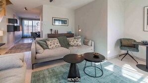 A modern living room with a sofa, two round coffee tables, and a dining area with a chair. - Smeysea - stylish apartment in Sint-Idesbald (Koksijde)