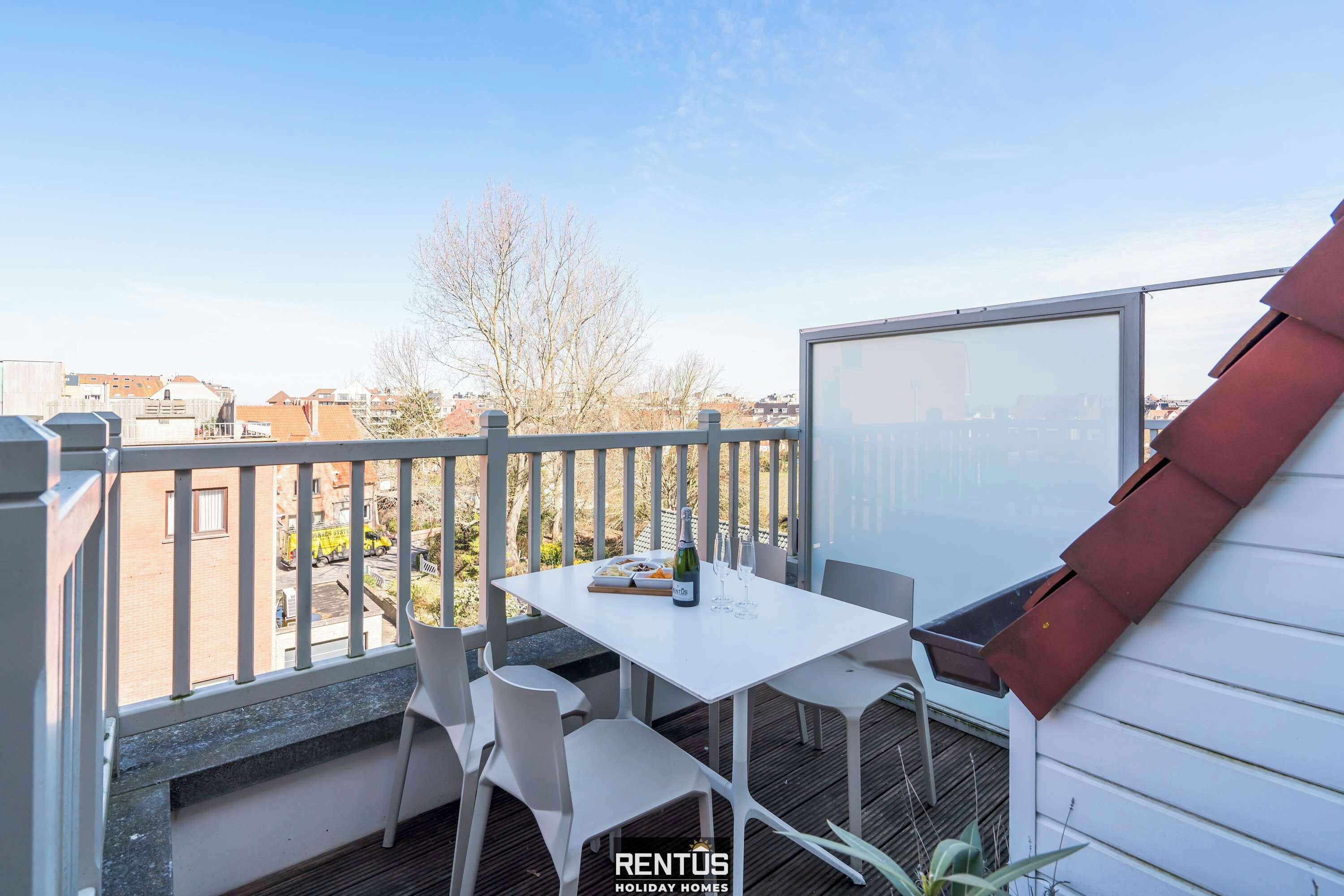 A balcony with a white table and chairs, a bottle of champagne, and a tray of snacks.