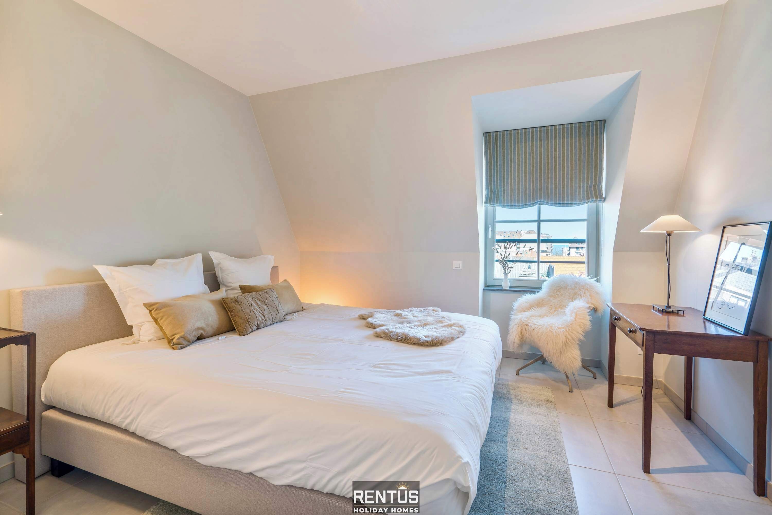 A bedroom with a large bed, a small desk, a chair, and a window with curtains.