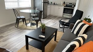 A modern living room with a dark brown sofa, a glass coffee table, and a dining area with a round table and chairs.