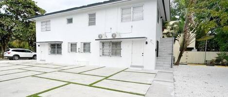 Un edificio blanco moderno de dos pisos con garaje, un acceso cubierto y un pequeño jardín delantero con una palmera.