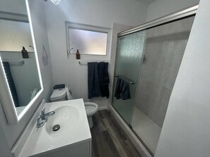 A compact bathroom with a white sink, a toilet, a mirror, and a glass shower enclosure. - Building next to CocoWalk & Brickell (Miami)