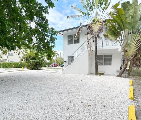 A two-story building with a white exterior, a staircase leading to the upper floor, and a gravel driveway. - Building next to CocoWalk & Brickell (Miami)