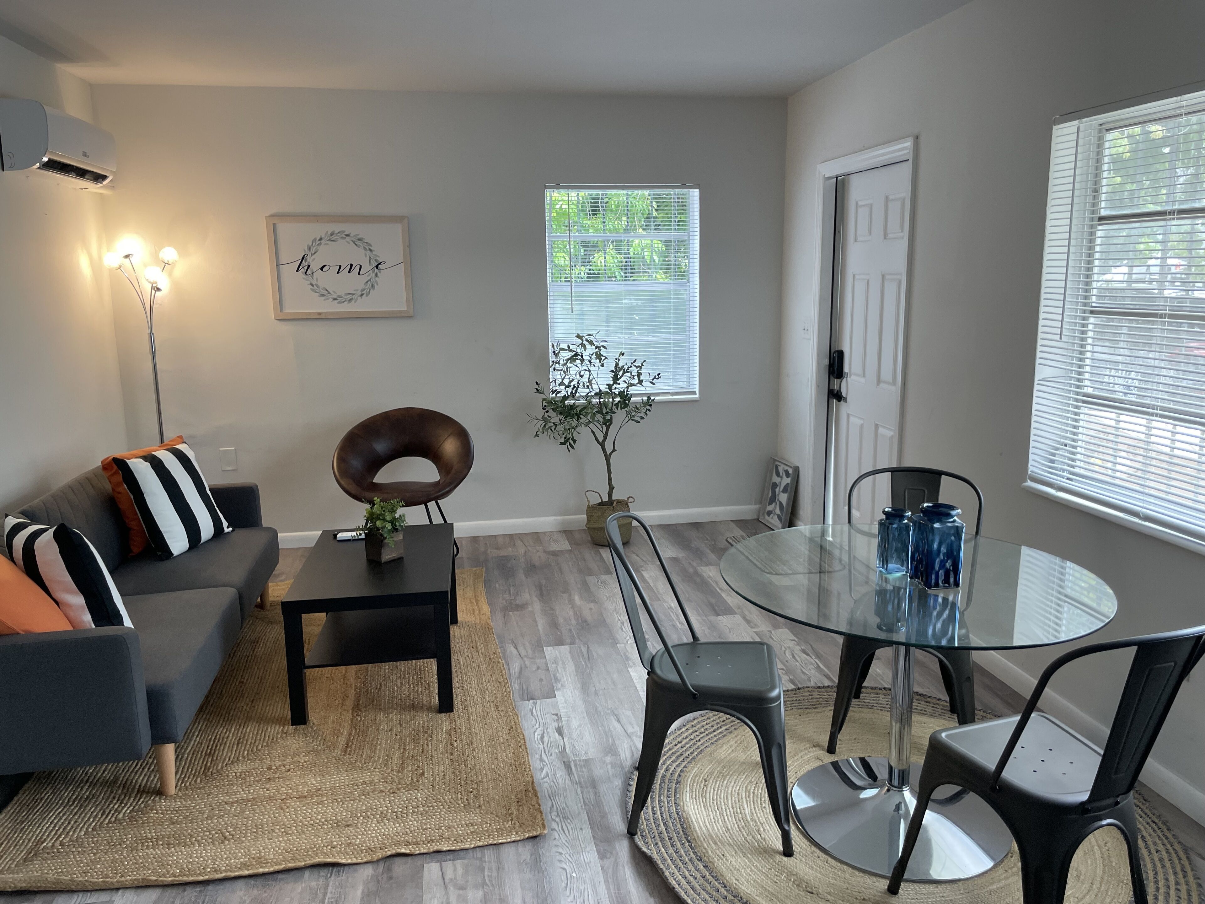 A modern living room with a glass dining table, dark grey sofa, and a decorative plant.
