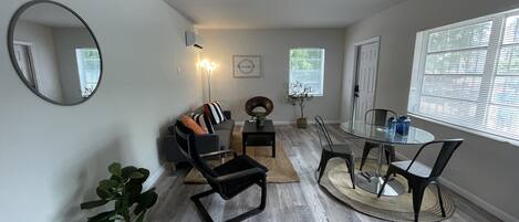 Una sala de estar moderna con un sofá gris, una mesa redonda de vidrio y un espejo grande.