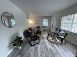 Una sala de estar moderna con un sofá gris, una mesa redonda de vidrio y un espejo grande.