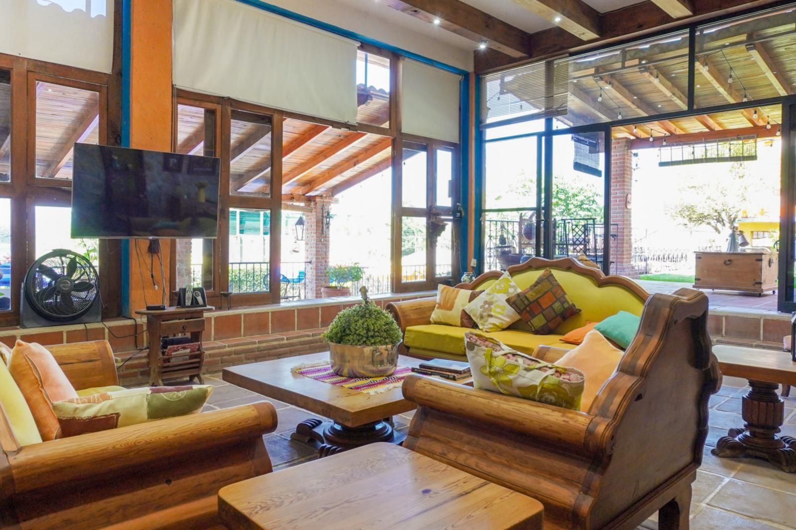 A spacious indoor seating area with wooden furniture, a flat-screen TV, and large windows offering views of the outdoors.