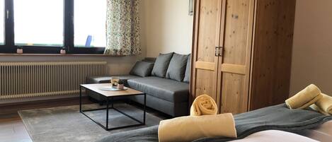 Une chambre d’hôtel avec un lit, un canapé, une armoire en bois, un radiateur et une fenêtre avec des rideaux.