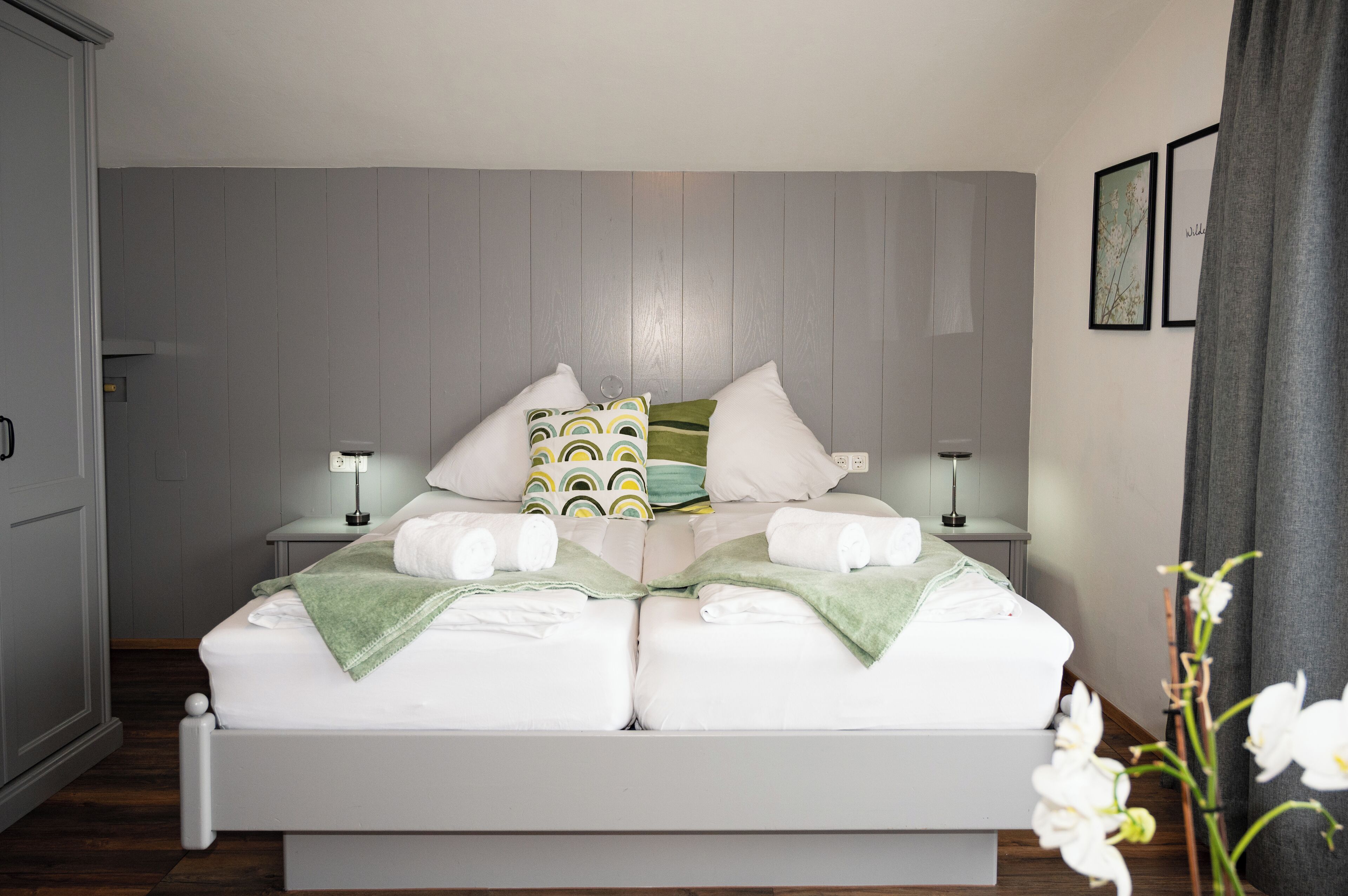 A neatly made bed with white linens and green throw blankets, two bedside tables with lamps, and a grey wooden headboard.
