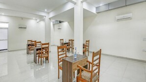 A spacious, well-lit room with a central wooden table surrounded by chairs, air conditioning units on the walls, and a tiled floor. - Hotel Collection Inn (Gurugram)