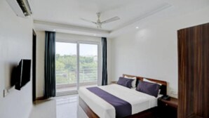A modern bedroom with a large bed, a flat-screen TV, and a view of greenery outside. - Hotel Collection Inn (Gurugram)
