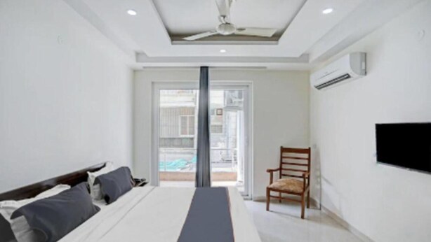 A hotel room with a bed, a chair, a television, and a view of the outside. - Hotel Collection Inn (Gurugram)