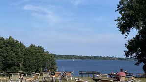 An outdoor seating area with wicker chairs and tables overlooking a lake. - Apartment flying stag (Bäk)