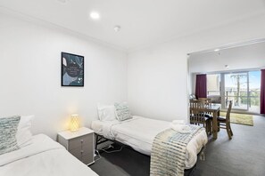 Two single beds with white bedding, a bedside table, and a framed quote adorn this stylish room with a city view.
