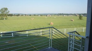 Une vue depuis un balcon donnant sur un champ verdoyant, avec des bottes de foin et une clôture blanche.