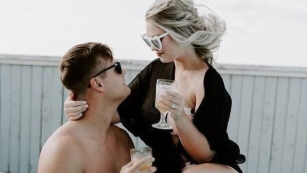 Un homme et une femme sont assis au bord d’une piscine, chacun tenant un verre à la main.