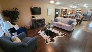 Un salon comprenant un canapé, un fauteuil et une table basse. Un téléviseur est fixé au mur et un ventilateur de plafond est installé.