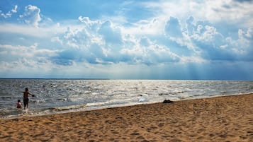 Ein Strand mit Sand und Wasser, bewölkter Himmel und eine Person im Wasser.
