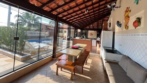 Eine überdachte Terrasse mit Pool, Holzmöbeln, Küchenbereich und dekorativer Wandgestaltung.