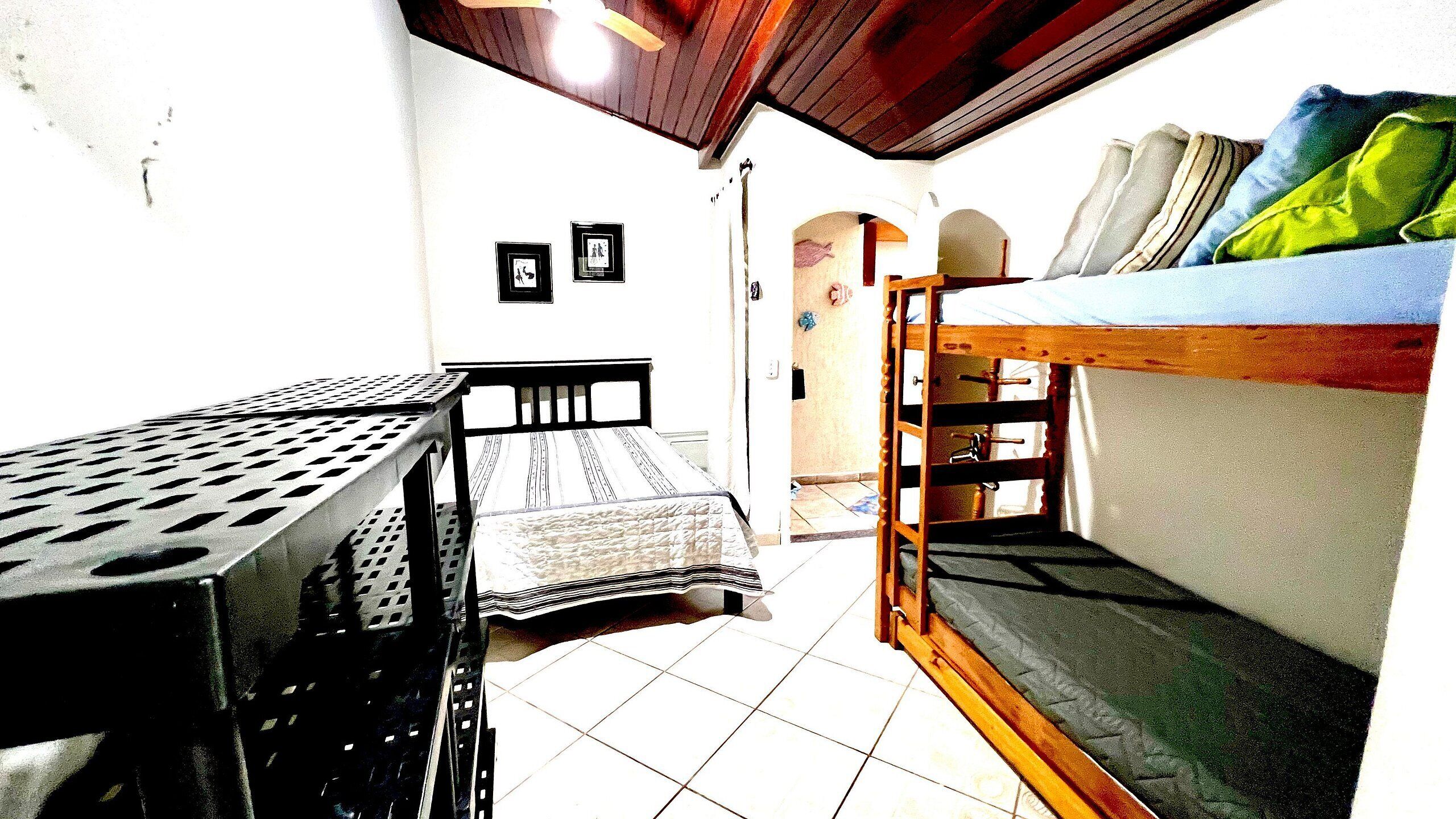 A small, compact room with a bunk bed, a single bed, and a metal table.
