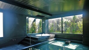 A modern indoor swimming pool with a glass enclosure, a hot tub, and a view of greenery outside. - OYADOKOTOBUKI (Shinonsen)