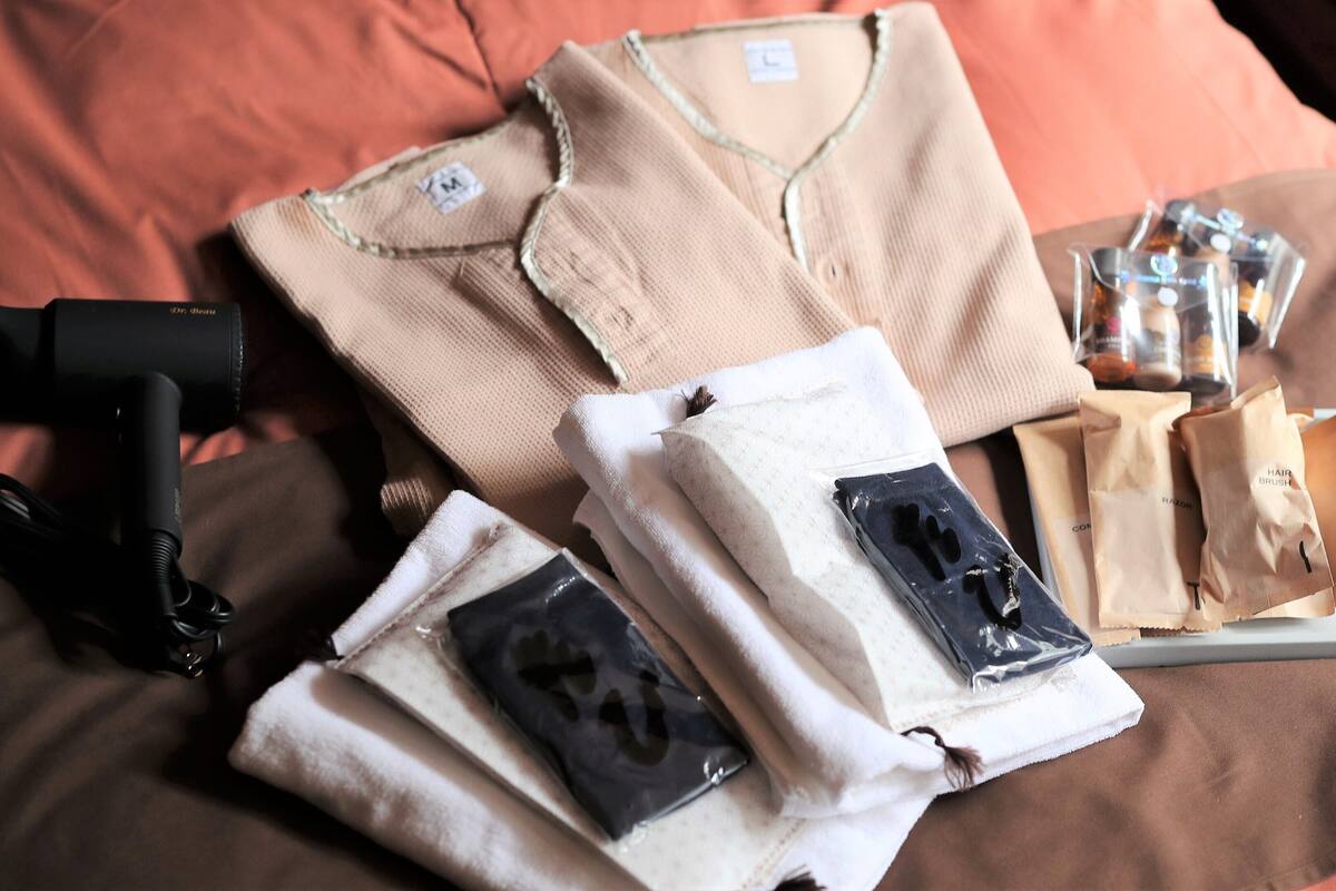 A neatly arranged bed with a brown pillow, a folded beige shirt, a black hairdryer, and several toiletry bags.