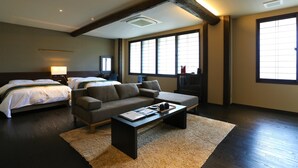 A modern hotel room with a large bed, a sofa, a coffee table, and a view of the city through large windows. - OYADOKOTOBUKI (Shinonsen)