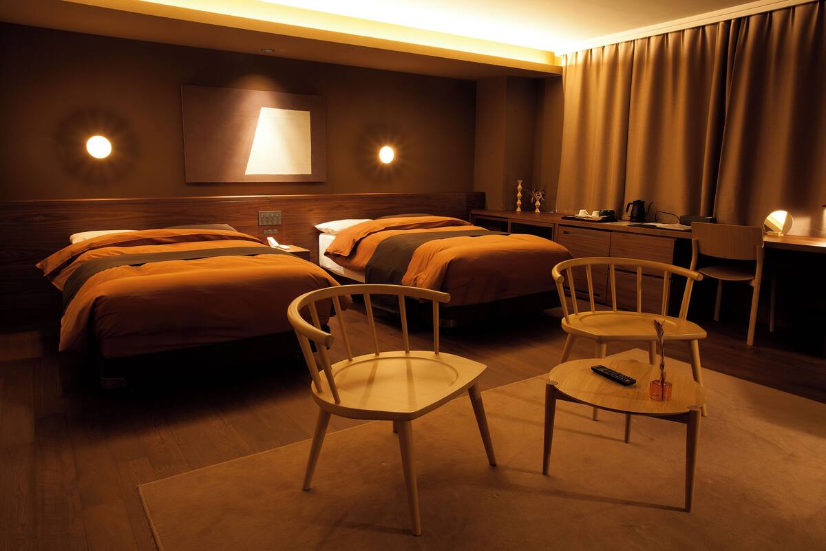 A hotel room with two beds, a desk, two chairs, and a TV.