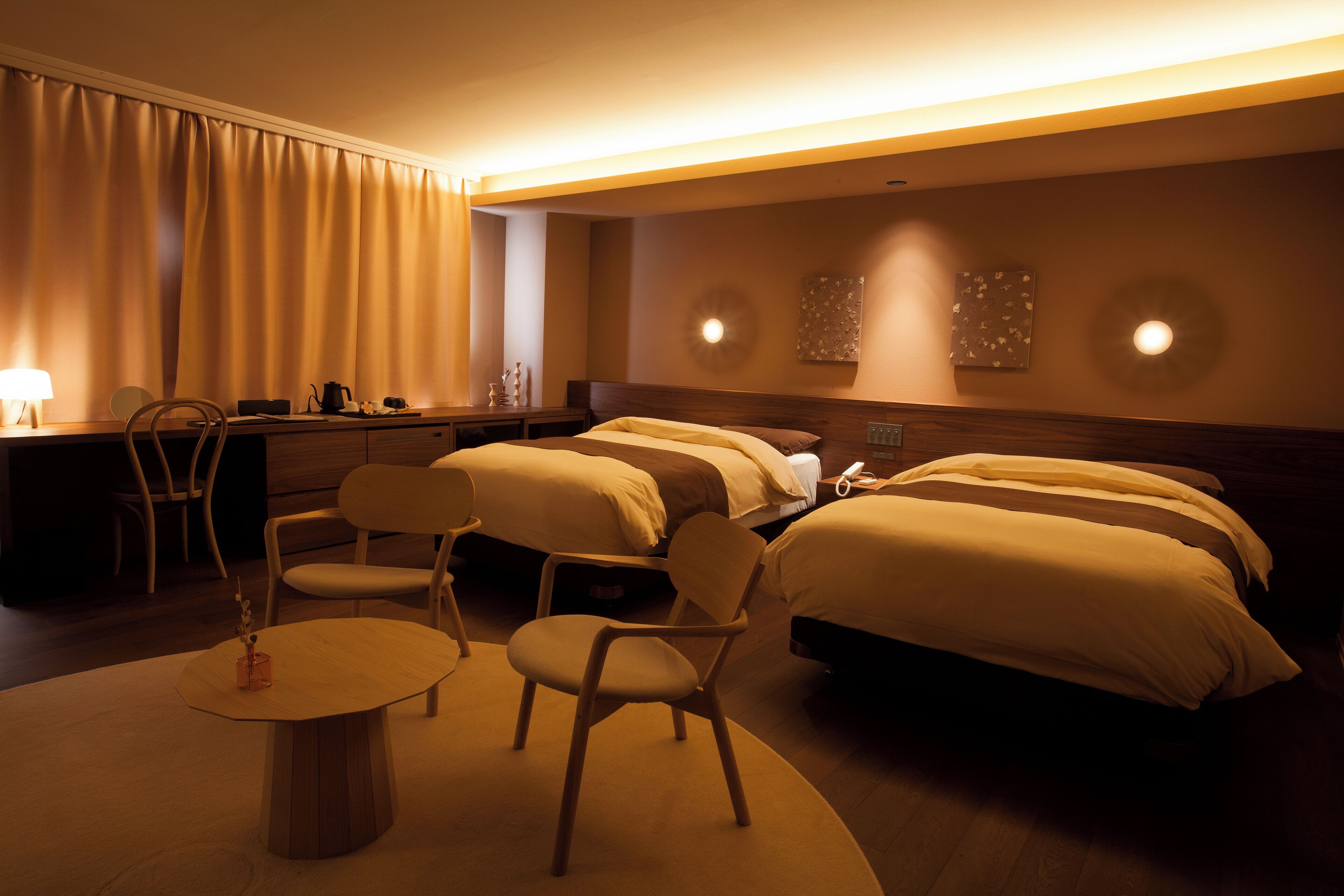 A hotel room with two beds, a desk, a chair, and a small table.