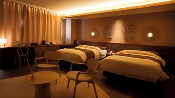 A hotel room with two beds, a desk, a chair, and a small table.