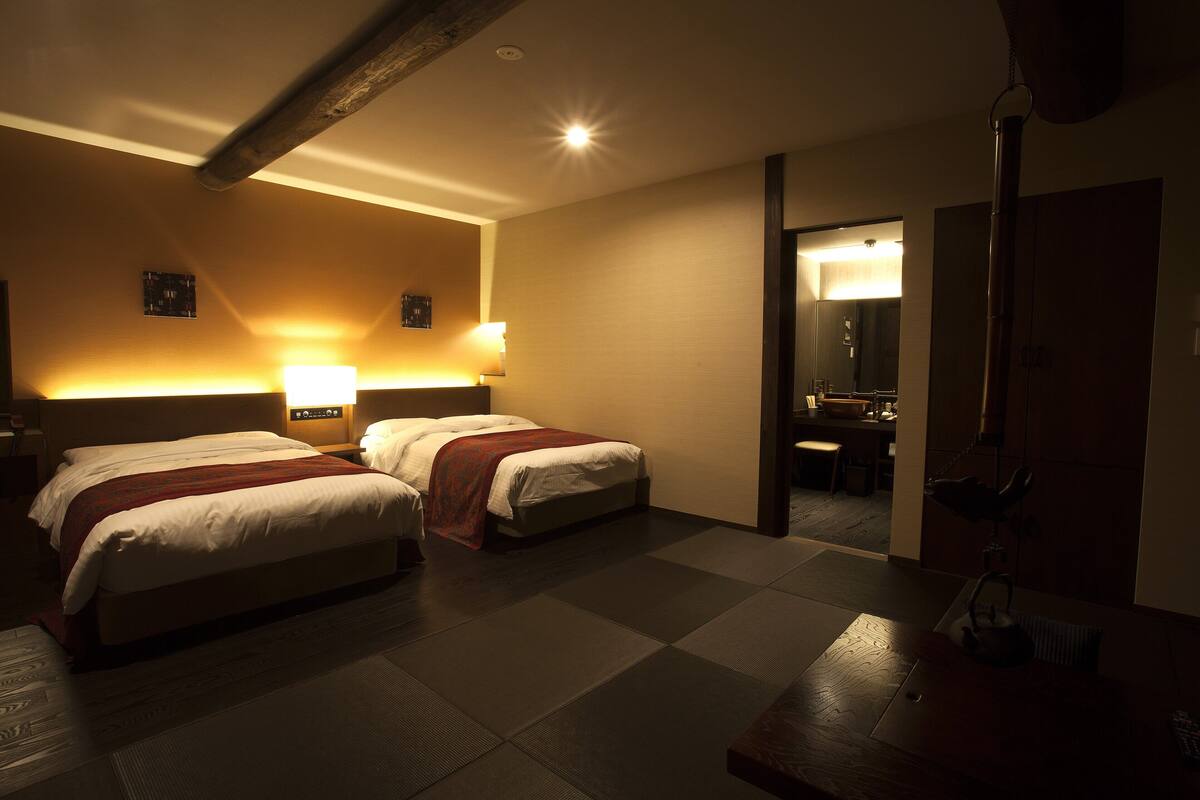 A hotel room with two beds, a desk, a chair, a mirror, and a bathroom visible through an open door.