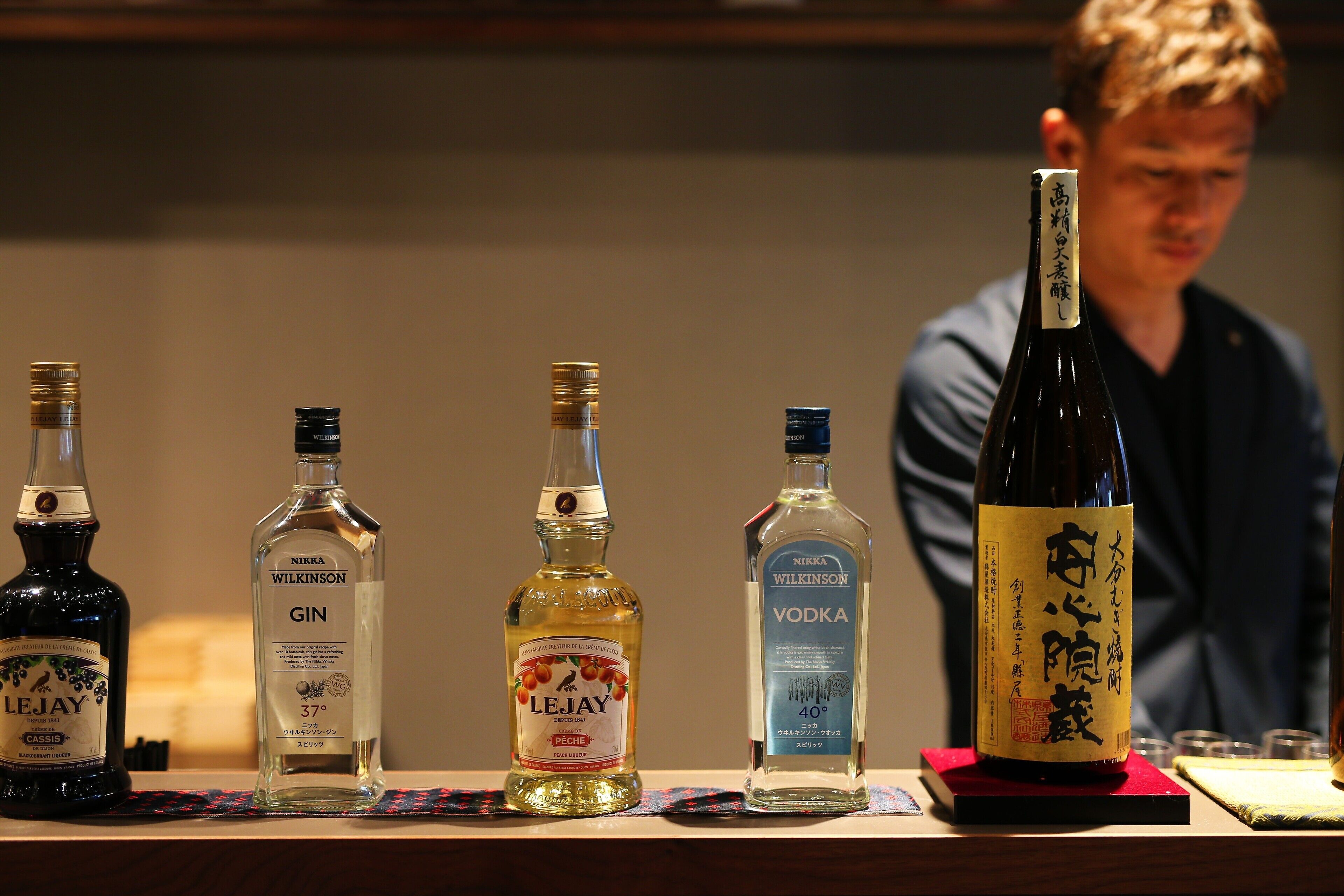 Four bottles of alcohol on a table with a person in the background.
