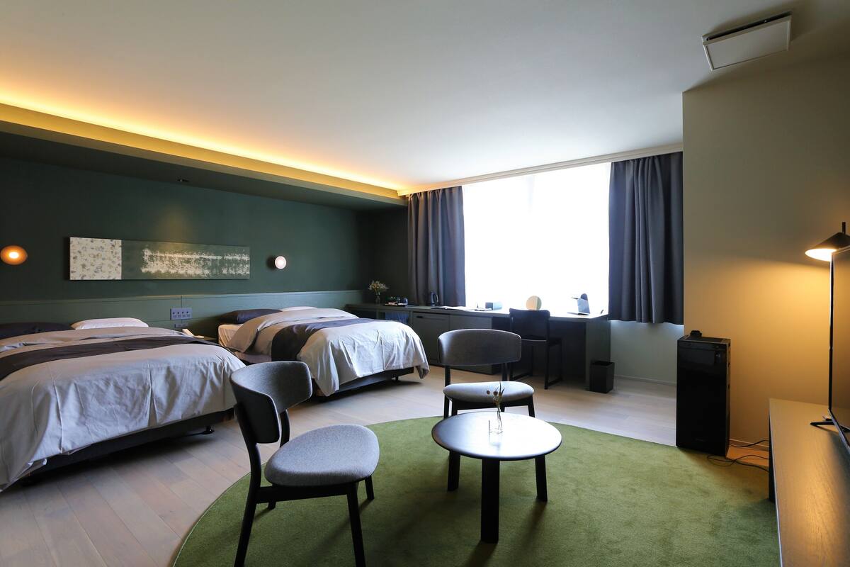 A hotel room with two beds, a desk, a chair, a small table, and a TV.