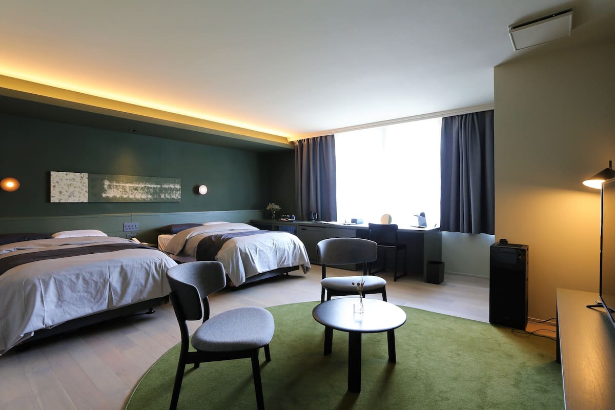 Habitación de hotel con dos camas, un escritorio, una silla, una mesita y un televisor.