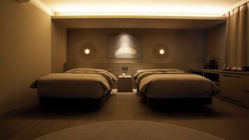A hotel room with two beds, a nightstand, and a desk with a lamp.