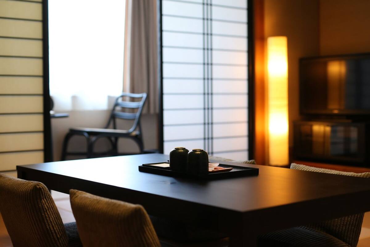A modern hotel room with a large window, a dining table with two chairs, and a television in the corner.