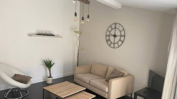 A modern living room with a sofa, a coffee table, a chair, a floor lamp, and a wall clock. - Appartement en Duplex Centre Historique (Montpellier)