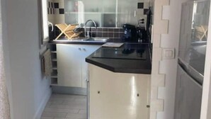 A compact kitchen with white cabinets, a black countertop, and a built-in oven. - Appartement en Duplex Centre Historique (Montpellier)