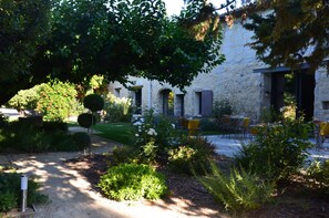 Un patio con asientos al aire libre, rodeado de vegetación y un edificio de piedra con arcos.