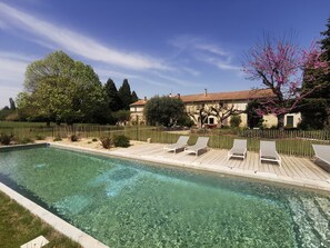 Una piscina cristalina con sillones de descanso, rodeada por una terraza de madera y un muro de piedra.