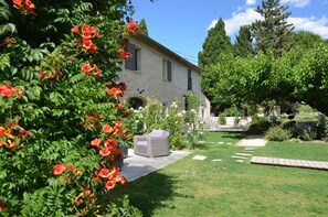 Un edificio de piedra con un jardín delantero, un sendero pavimentado y un césped.