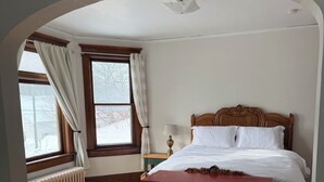 Una camera da letto con pavimento in legno, una cassettiera rossa, struttura del letto in legno, una finestra con tende e un termosifone.