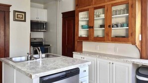 Una cucina con piano di lavoro in granito, elettrodomestici in acciaio inossidabile, mobili bassi bianchi e pensili in legno.