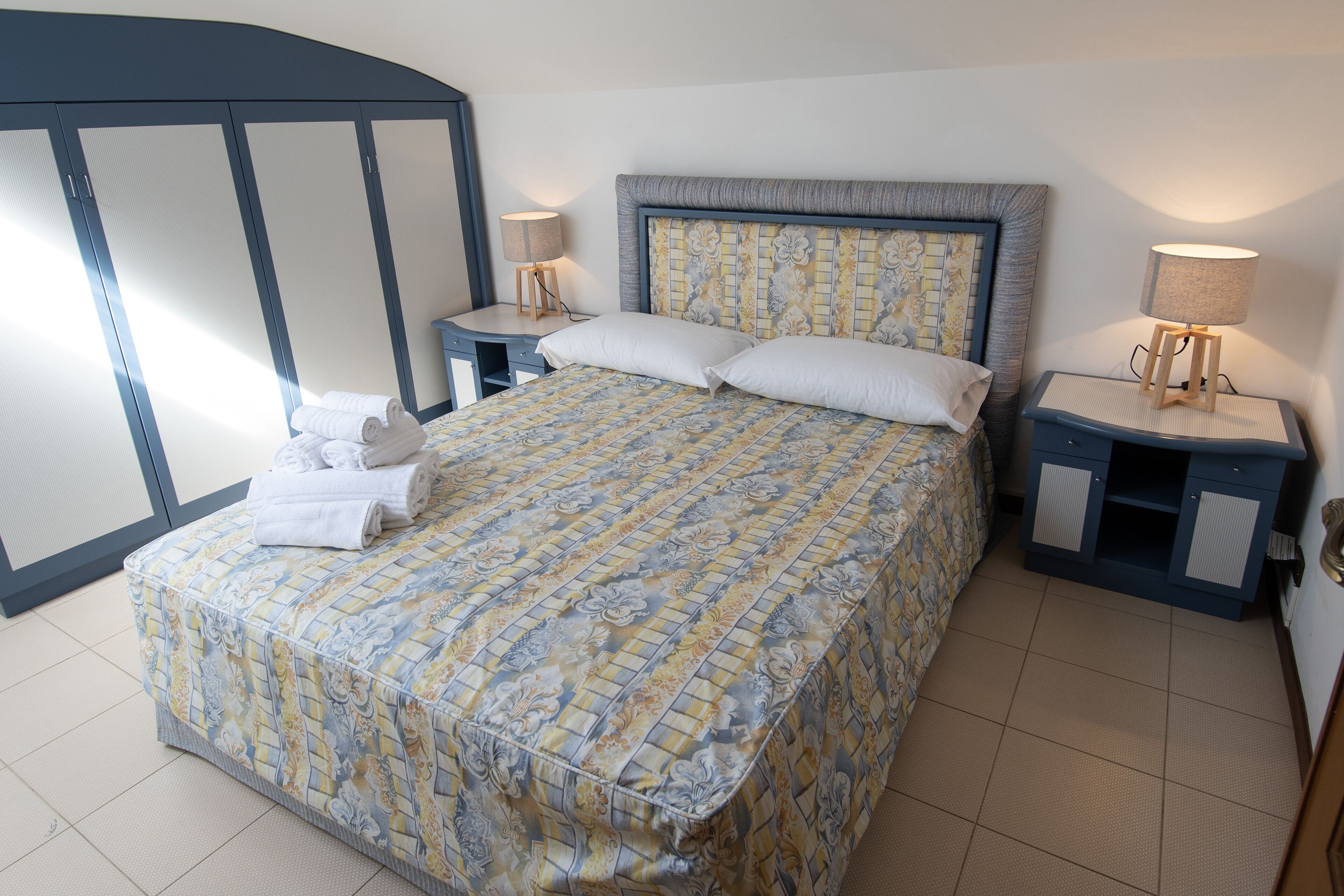 A neatly made bed with a patterned bedspread, two bedside tables with lamps, and a wardrobe with a mirrored door.