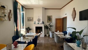 A dining area with a fireplace, multiple tables and chairs, and a large window with curtains.