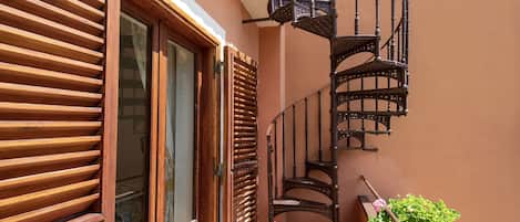 A spiral staircase with a wooden handrail and a metal balustrade, leading to an upper floor.