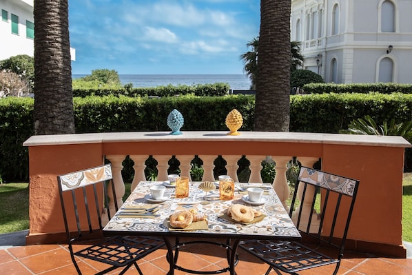 A table set for two with a view of the sea, palm trees, and a building in the background.