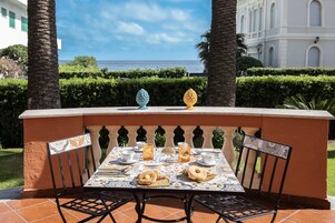 A table set for two with a view of the sea, palm trees, and a building in the background.