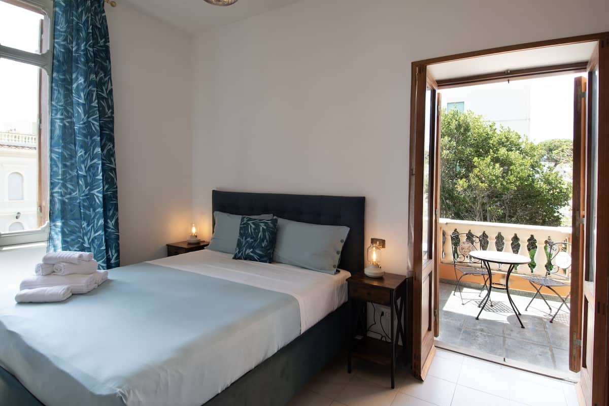 Une chambre à coucher comprenant un lit, des tables de chevet, un balcon avec une table et des chaises, et une vue sur l’extérieur.