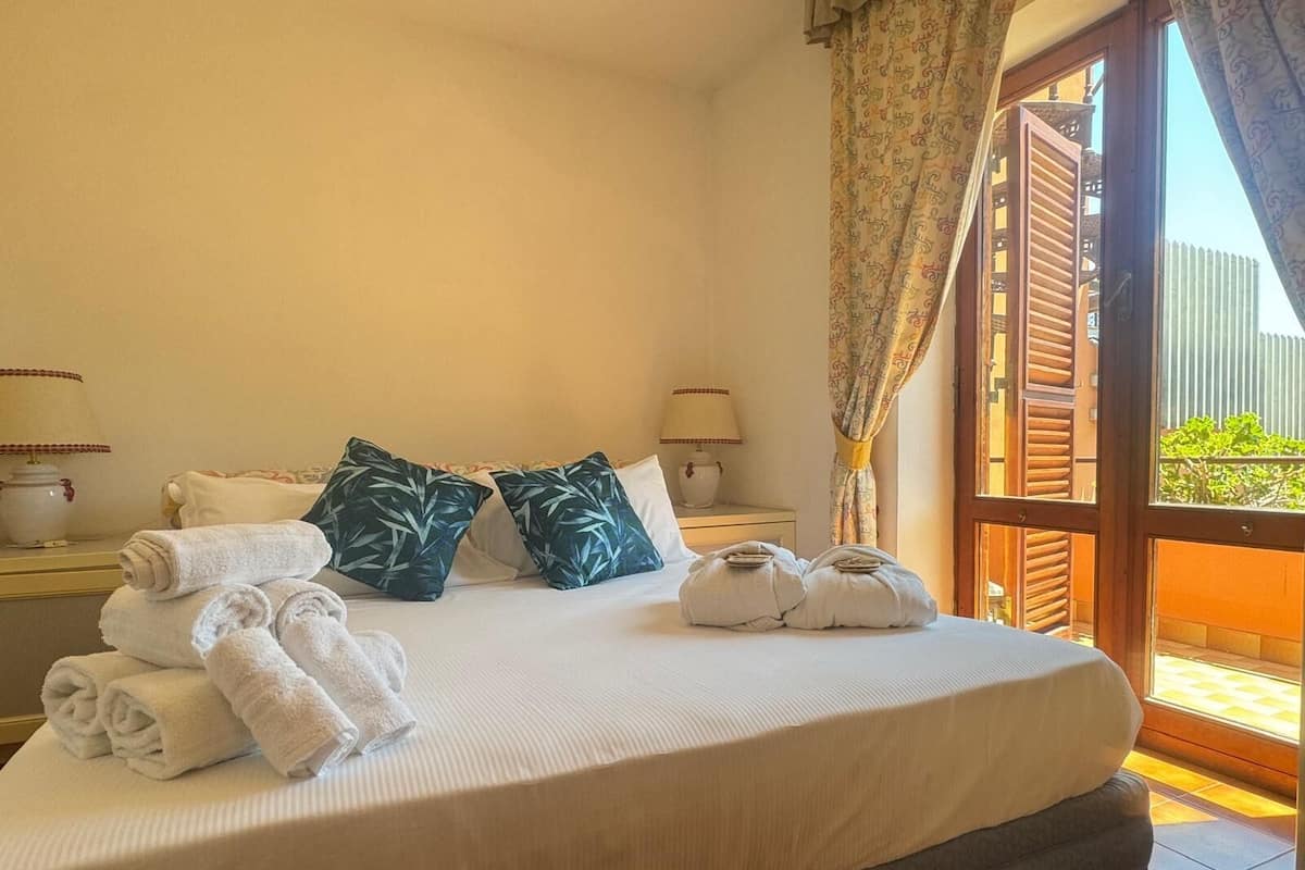 Une chambre d’hôtel avec un grand lit, deux tables de chevet, une fenêtre avec des rideaux et une vue sur la verdure.